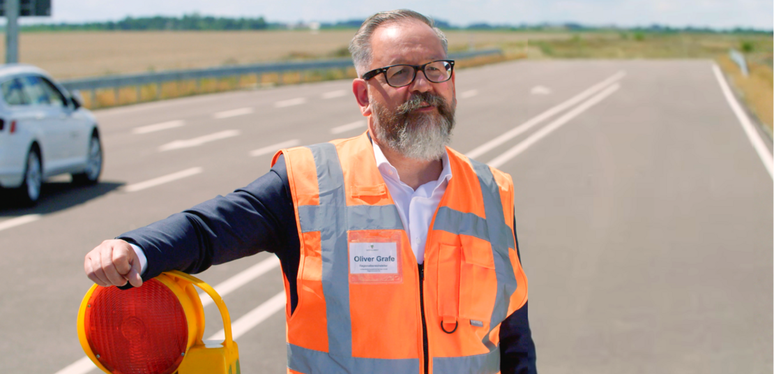 Ein Kollege der Landesstraßenbaubehörde Sachsen-Anhalt steht an einer Straße, den Arm auf eine Absperrbake gestützt. 